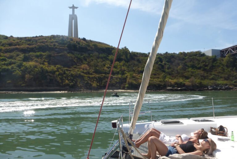 Duas pessoas deitadas na rede do catamaran e o Cristo Rei ao fundo